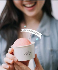 A woman holding a cup of pink ice cream with a “Piccoli Lotti” logo, celebrating a birthday, representing a free ice cream giveaway for birthdays.